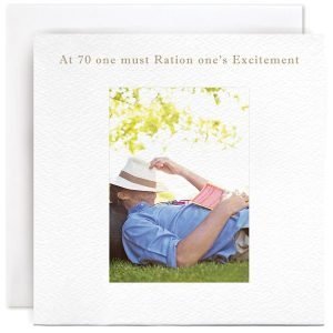 A white square card with a photographic image of a man lying on grass with a hat over his head and a book on his chest. The wording At 70 One Must Ration One's Excitement is printed above the image.