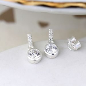 A pair of silver crystal drop earrings. The earrings have a silver bar with 3 cubic zirconia in the bar and a larger cubic zirconia at the end of the bar.