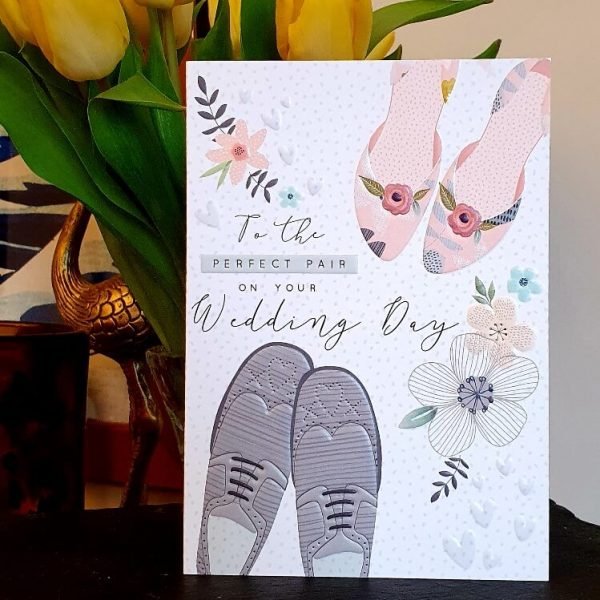 A beautiful embossed wedding card with a pair of men's shoes and ladie's shoes and delicate flowers and the words To the perfect pair on your wedding day.