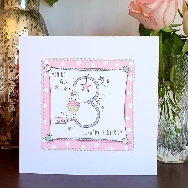 A 3rd birthday card in pinks with a big stripy 3 and birthday presents, stars and balloons. Hand finished with stitching and silver stars