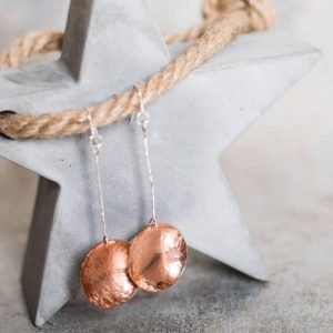 A pair of long drop earrings hand crafted from copper and sterling silver. A long silver wire with a hammered textured copper disc suspended from the end. Presented in a gift box