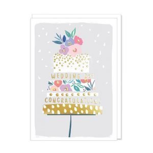 A wedding card with a contemporary illustration of a layered wedding cake with gold foil details and flowers in pinks and purples and wedding congratulations in gold writing