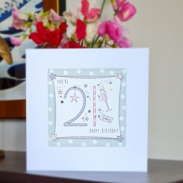 A 21st birthday card. A white card with a green spotty square stitched on to the card with a colourful hand drawn 21, little hand drawn stars and champagne flutes. You're 21 Happy Birthday