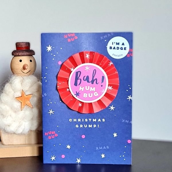 a Christmas card with a rosette badge that says bah hum bug.