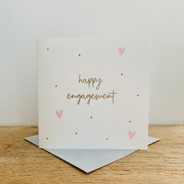 A square white card with gold spots and pink hearts on it and the words Happy Engagement in gold print