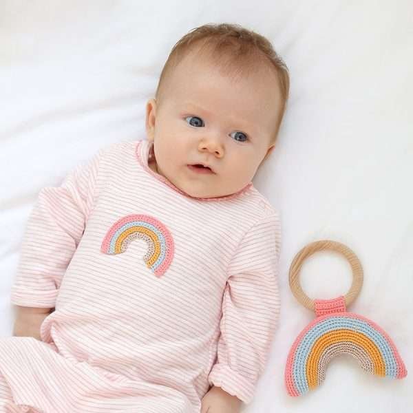 A pink and white striped cotton baby grow with a crochet rainbow motif worn by a baby