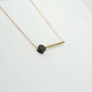 Bat and dot necklace. A black powder coated brass disc and a brass bar threaded onto a fine gold plated necklace