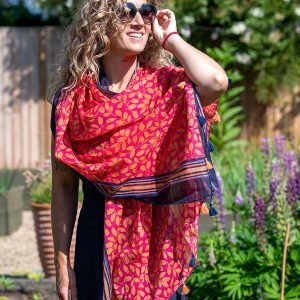 100% cotton scarf with a bright red and orange leaf print, edged with a navy striped border and finished with tassels at each end